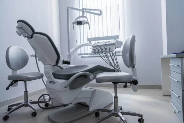 Modern dental treatment room featuring a high-tech dental chair, overhead light, and two adjustable patient chairs, emphasizing advanced periodontal care in a clean, bright environment.